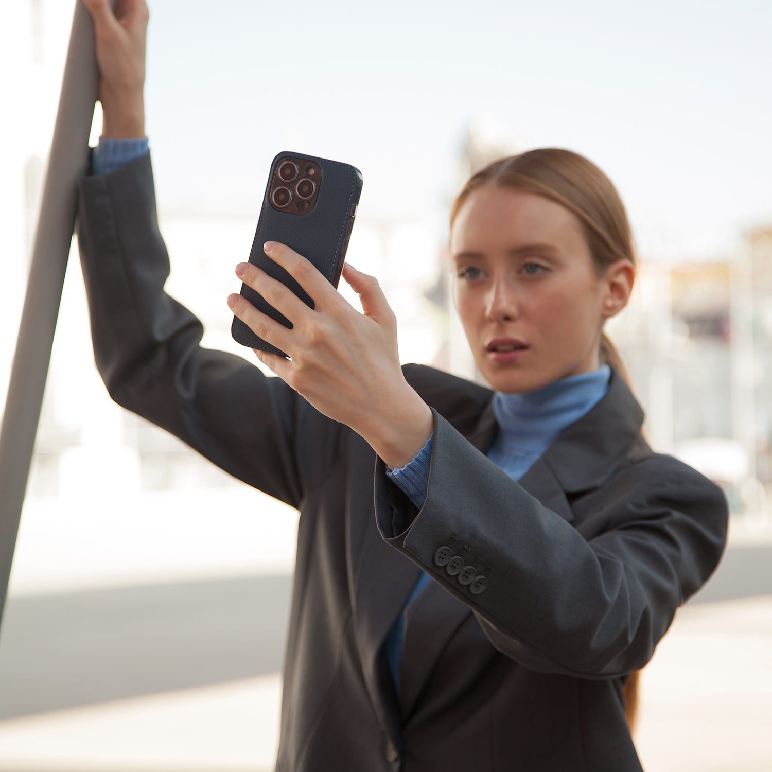 Red-haired woman holding iPhone 15 with Marcel Robert blue saffiano leather case
