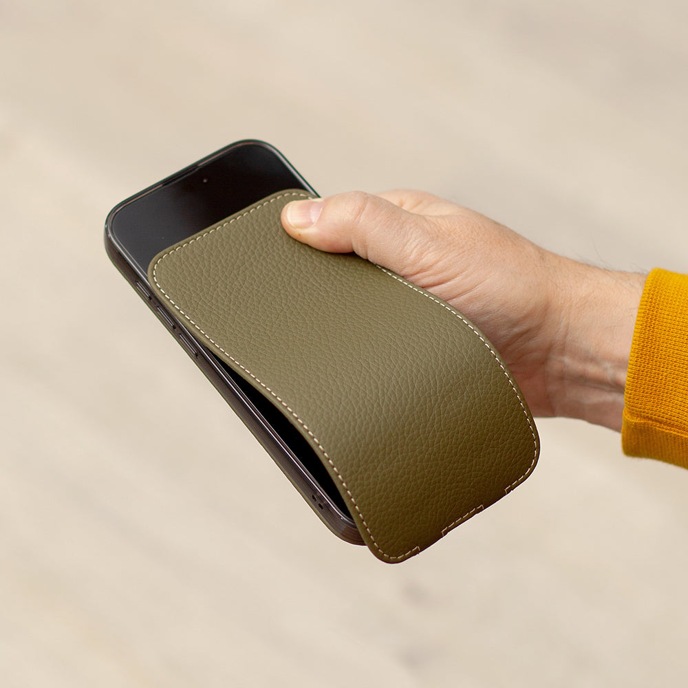 Person holding a phone in leather case with a brand logo, wearing a yellow shirt.