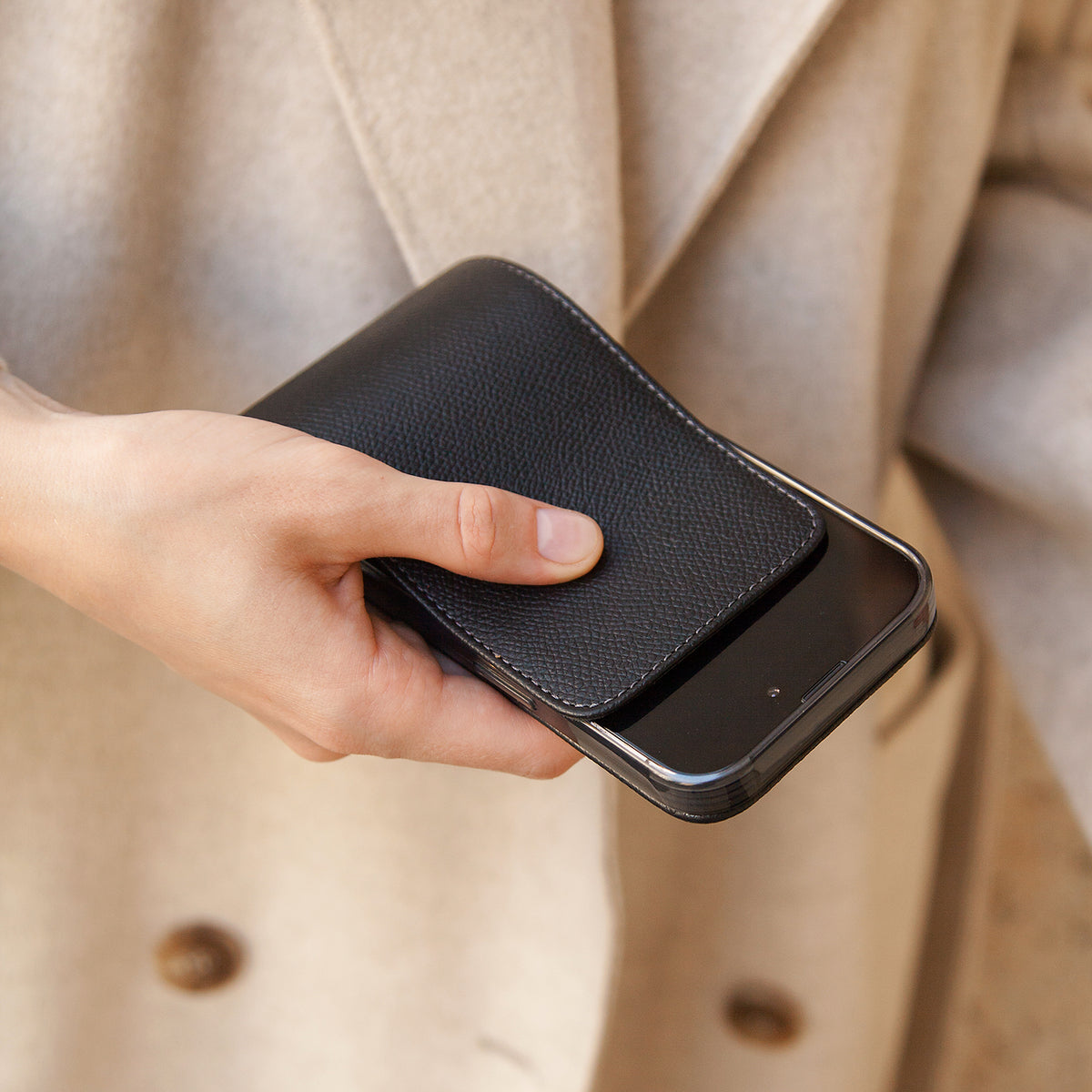 Black Epsom calfskin leather flip case for iPhone 15 Plus held in one hand, flap closed flat over the screen