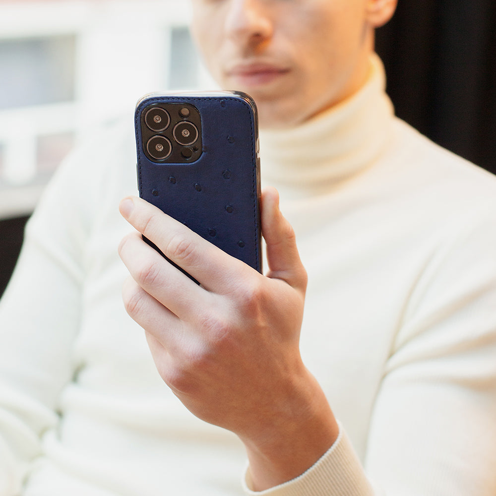 Man in white turtleneck holding iPhone 13 Pro with Marcel Robert blue ostrich leather case