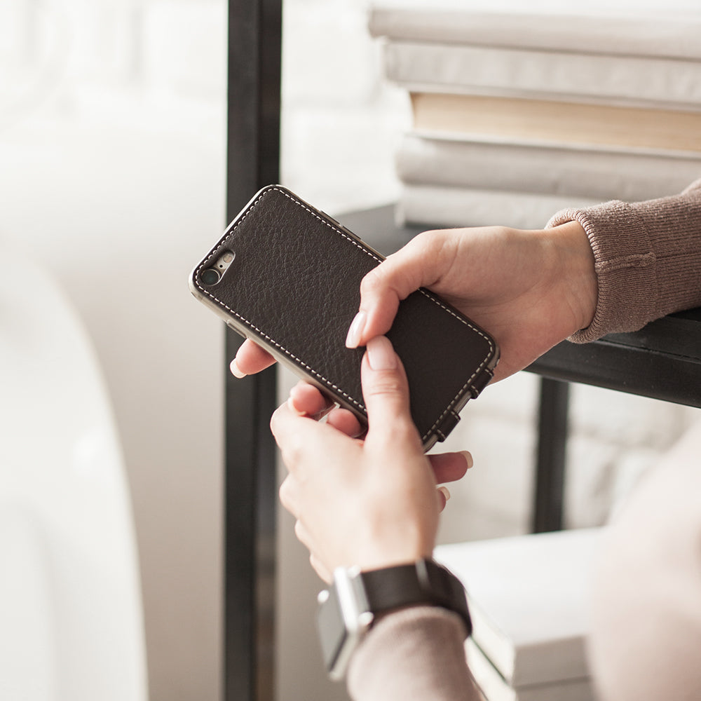 Brown leather flip case for iPhone SE in woman's hands, near a bookshelf