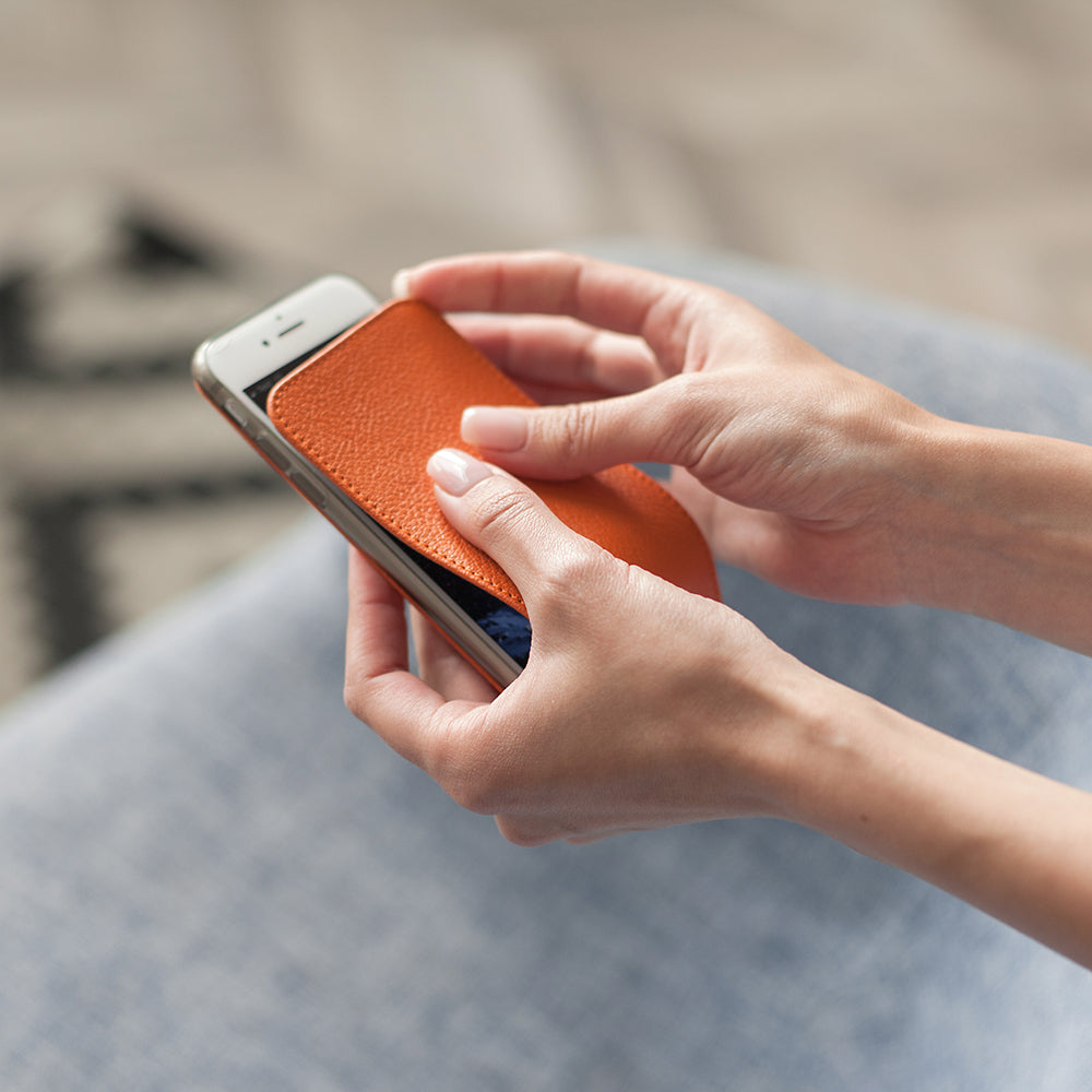 Orange leather flip case for iPhone SE in woman's hands, fitting the case onto the phone