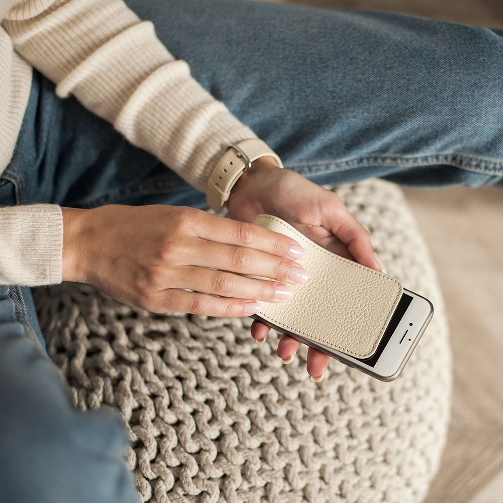 Cream leather flip case for iPhone SE in woman's hands, sitting on a knitted pouf