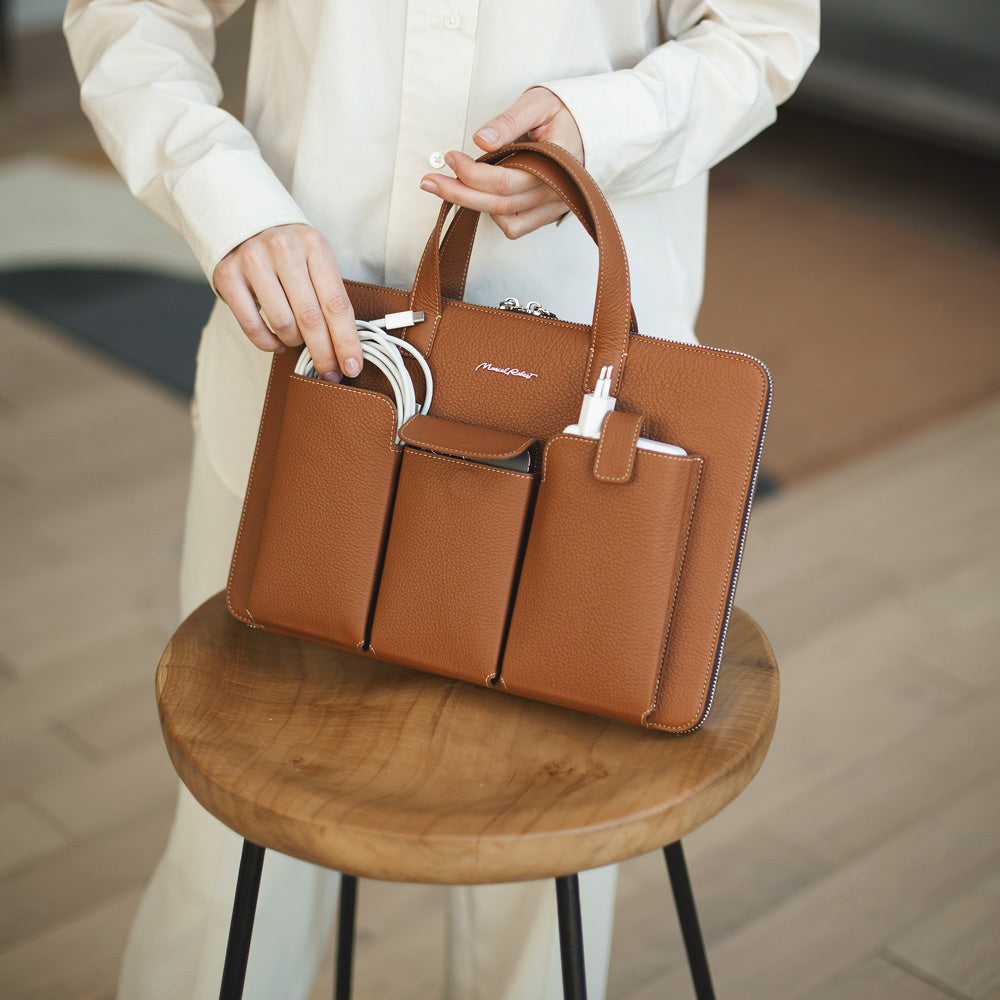 Gold 14 inch leather laptop bag with structured exterior pockets displayed on wooden stool