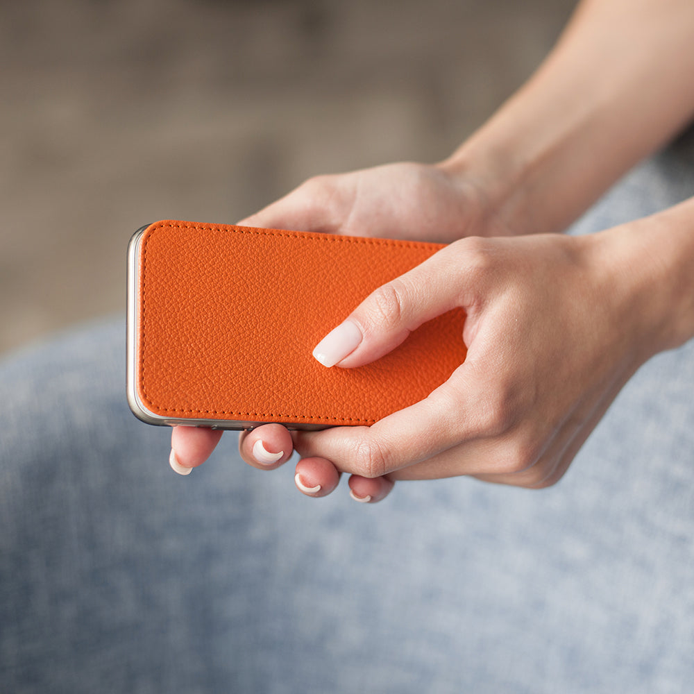 Orange leather flip case for iPhone XS Max in woman's hand, close-up of the closed cover