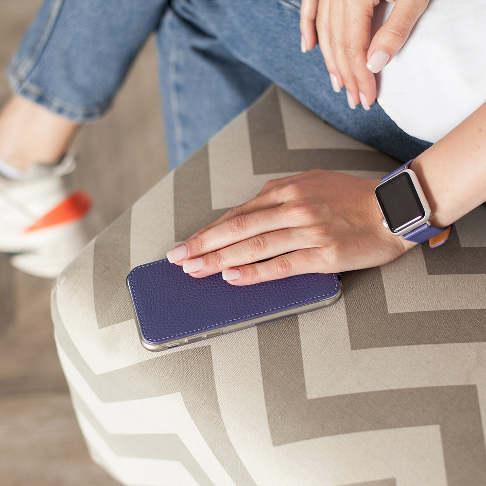 Purple leather flip case for iPhone SE in woman's hand, resting on a chair