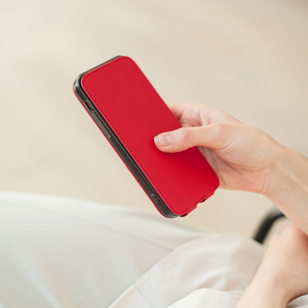 Red calfskin leather flip case for iPhone 15 held in one hand, flap closed flat over the screen