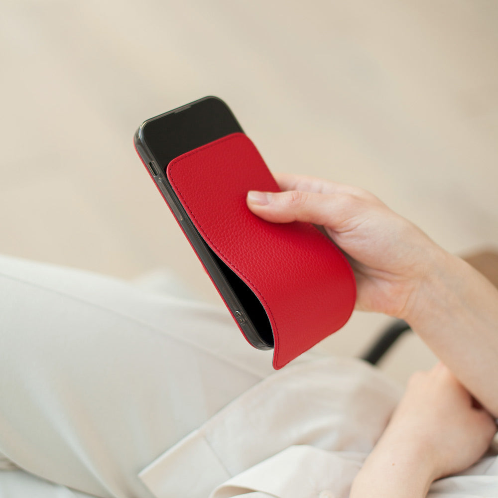Red calfskin leather flip case for iPhone 15 held in one hand, flap folded open behind the phone