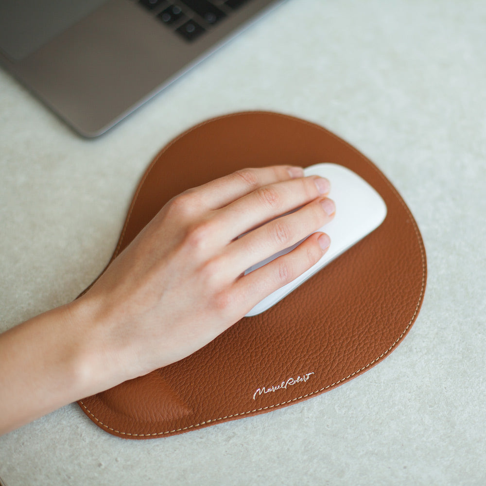 Hand on a mouse resting on a gold leather mouse pad next to a laptop