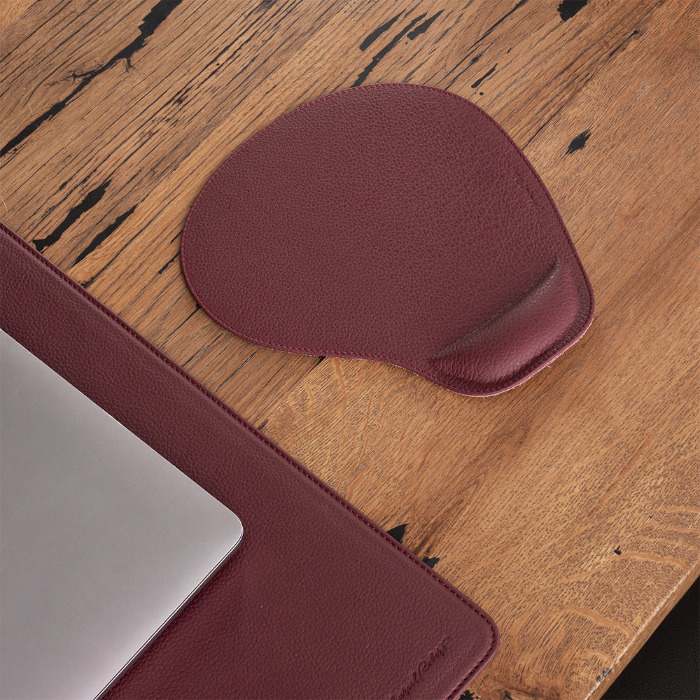 Bordeaux leather mouse pad on a wooden desk beside a laptop