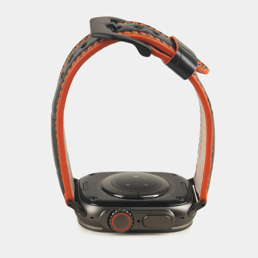 Apple Watch Ultra 49 mm in black alligator leather with orange stitching and edge, with black adapters and buckle | watch case on bottom to see the strap profile and the orange dyed edge