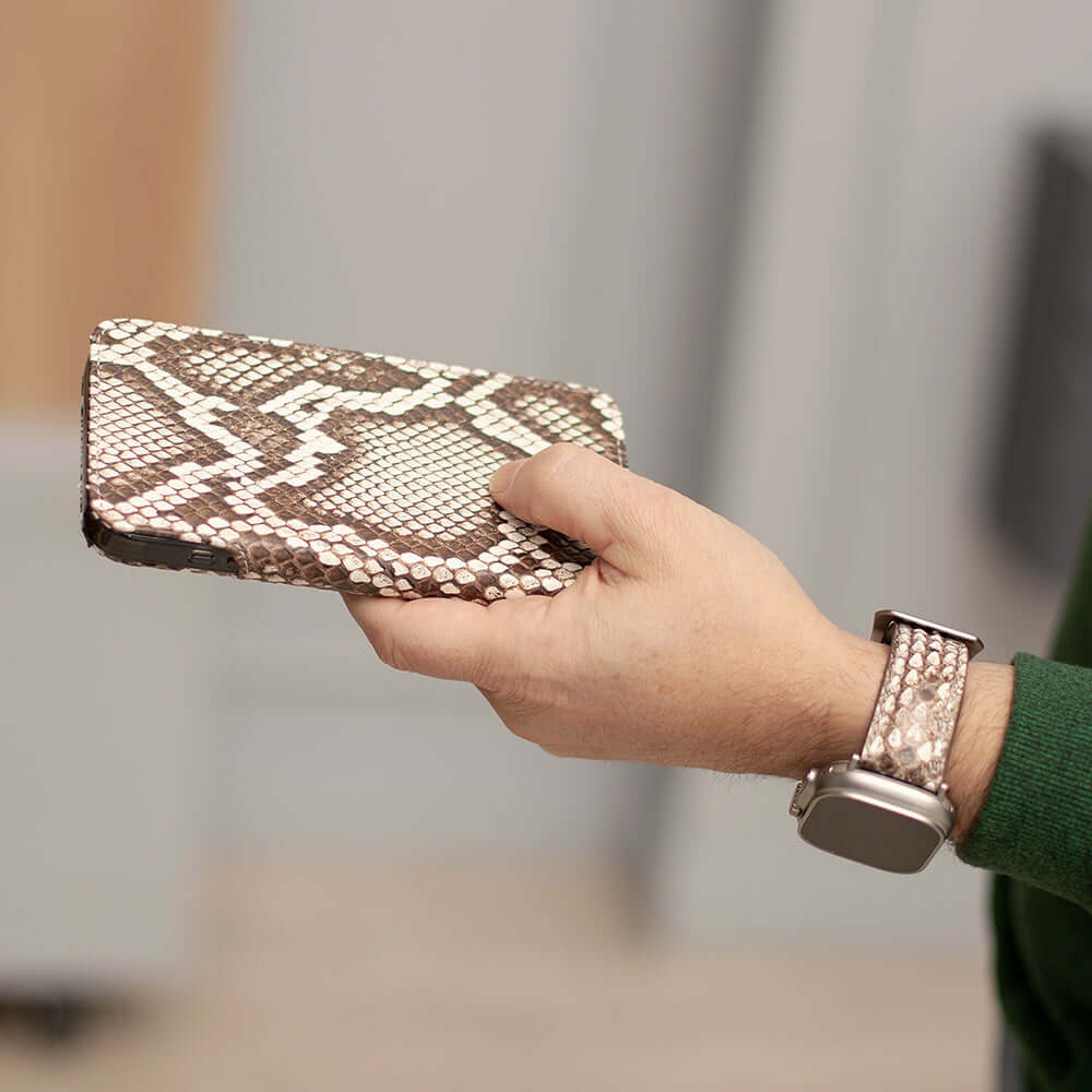 Hand holding iphone in snake skin patterned wallet case with matching strap of apple watch on blurred background