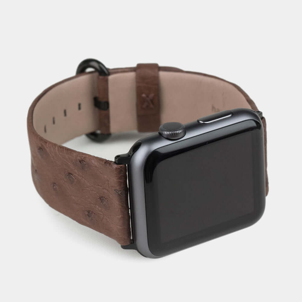 Strap for the Apple Watch 41/42 mm in brown ostrich leather, with black adapters and buckle | watch case on bottom to see leather texture, inner lining and the buckle