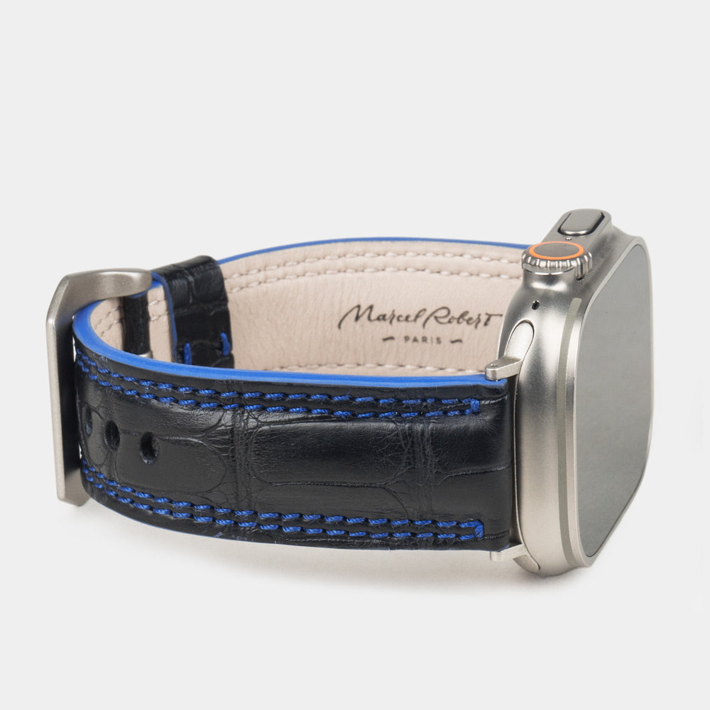 Apple Watch Ultra 49 mm in black alligator leather with blue stitching and edge, with titanium adapters and buckle | 3/4 view showing the leather inner lining and the Marcel Robert signature