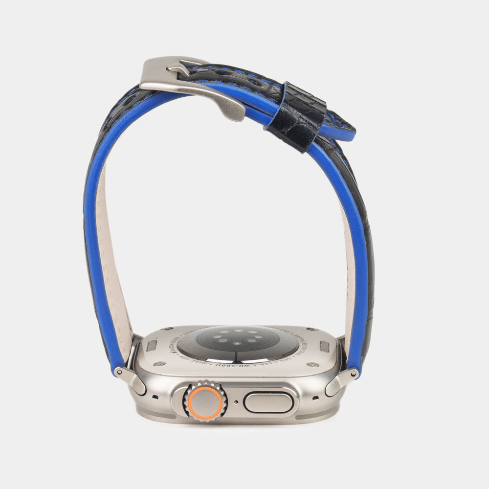Apple Watch Ultra 49 mm in black alligator leather with blue stitching and edge, with titanium adapters and buckle | watch case on bottom to see the blue dyed edge