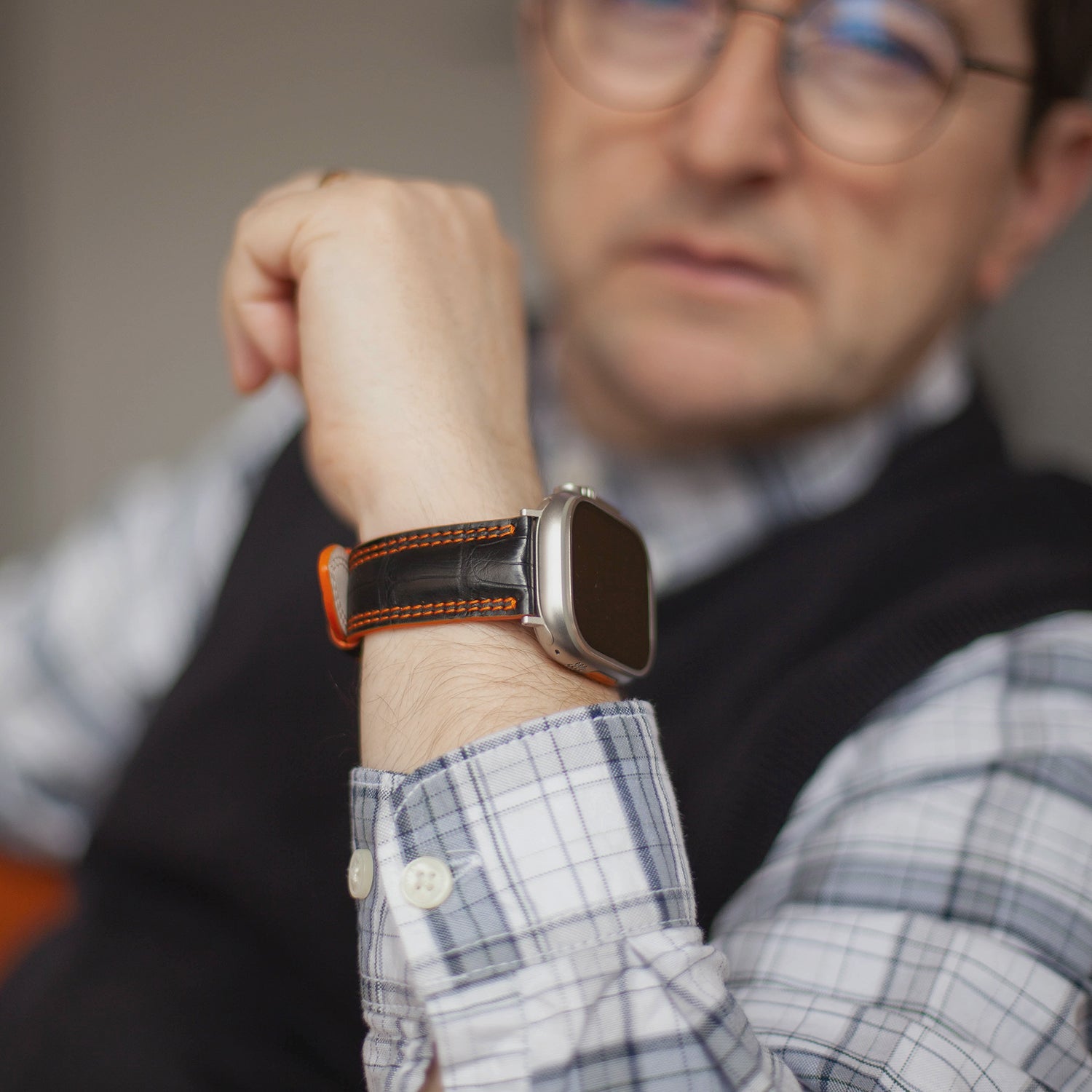 Apple Watch Ultra 49 mm in black alligator leather with orange stitching and edge, with titanium adapters and buckle | lifestyle photo, the strap worn on a man's wrist