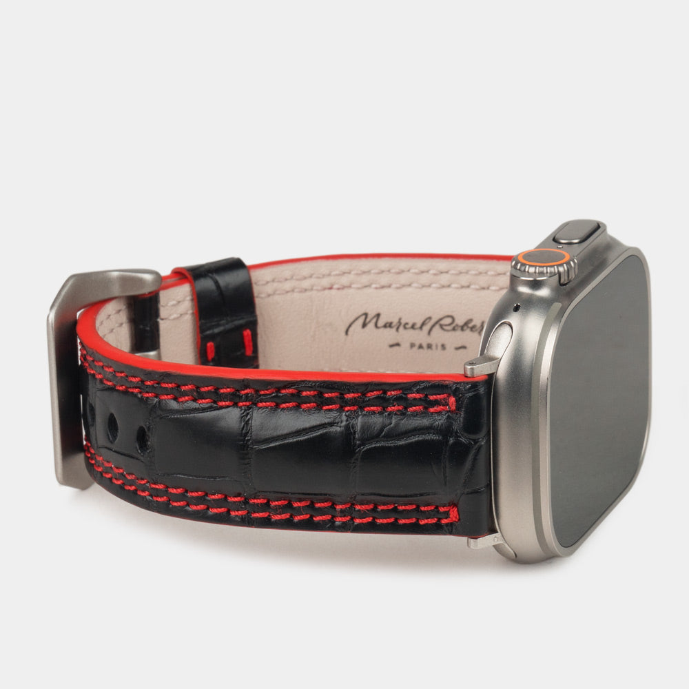 Apple Watch Ultra 49 mm in black alligator leather with red stitching and edge, with titanium adapters and buckle | 3/4 view showing the leather inner lining and the Marcel Robert signature
