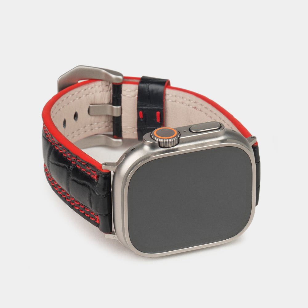 Apple Watch Ultra 49 mm in black alligator leather with red stitching and edge, with titanium adapters and buckle | 3/4 front view showing the titanium watch case and the square scales of the leather