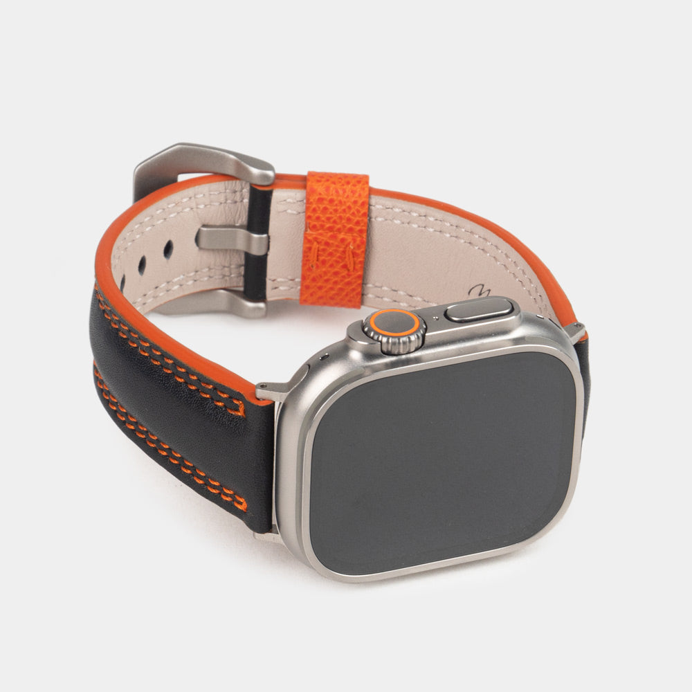 Men's Apple Watch Ultra band 49mm in black smooth calfskin leather with orange edge finish and its titanium color adapters - front dial view
