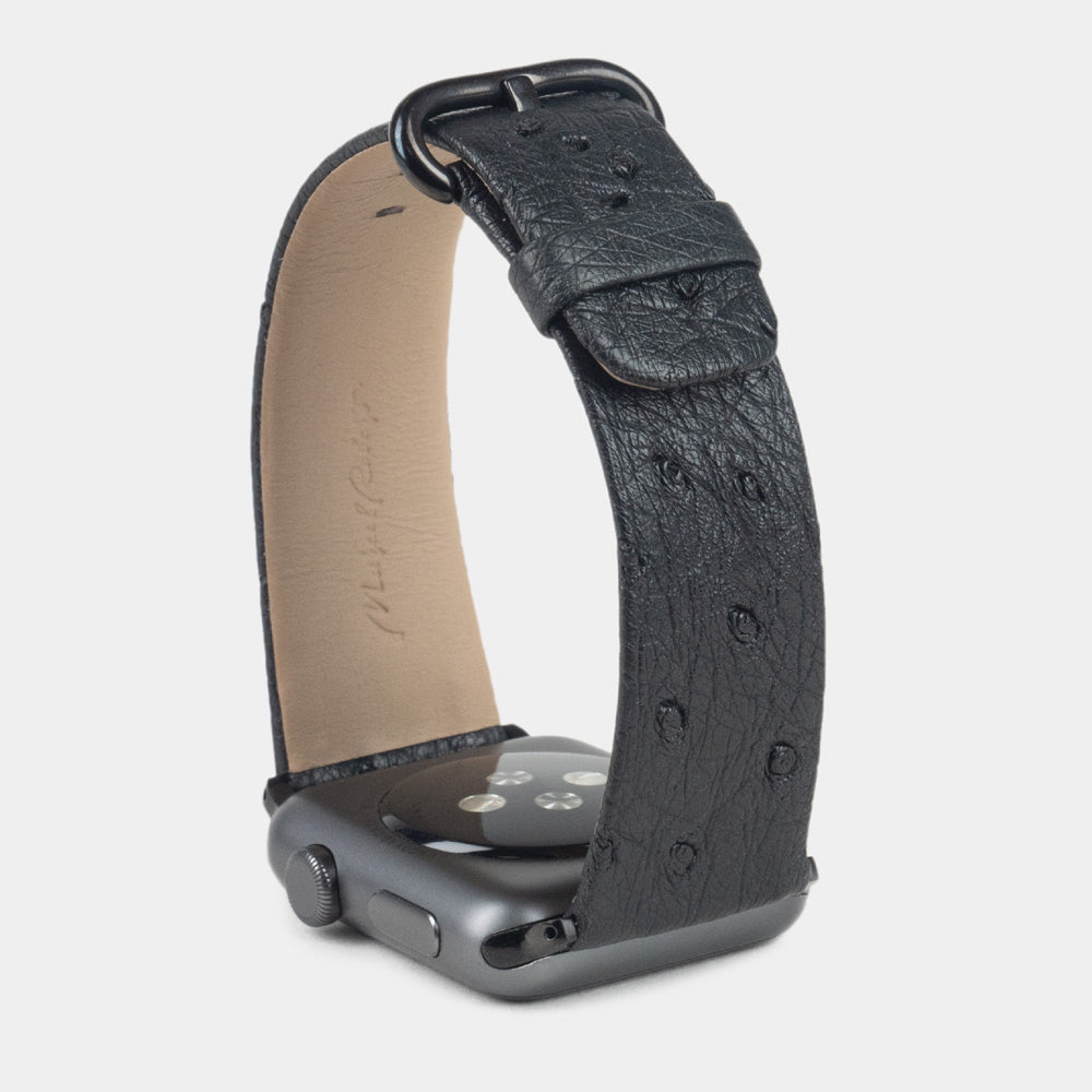 Strap for the Apple Watch 41/42 mm in black ostrich leather, with black adapters and buckle | watch case on bottom to see leather texture, inner lining and the buckle