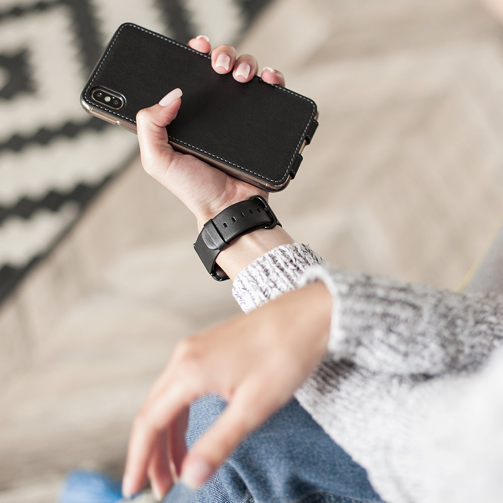 Black leather flip case for iPhone XS Max in woman's hand, back view showing the smooth leather finish