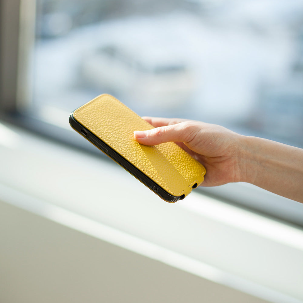 Yellow calfskin leather flip case for iPhone 15 Plus held in one hand, flap closed flat over the screen