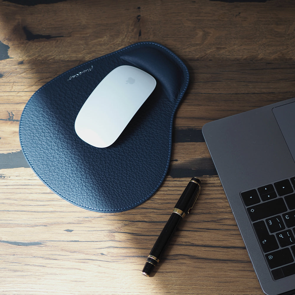 Blue leather mouse pad with mouse on a wooden desk next to a laptop