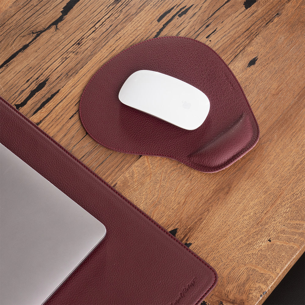 Bordeaux leather mouse pad with mouse on a wooden desk, laptop alongside