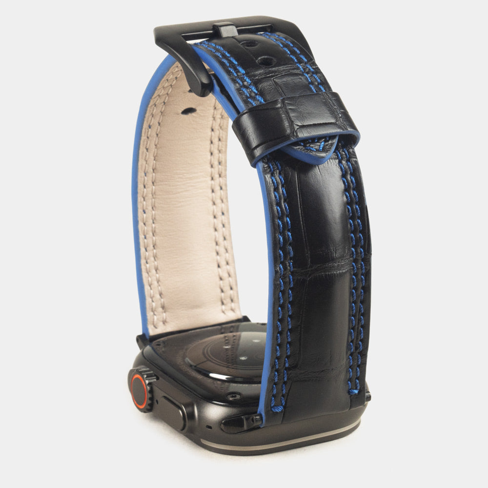 Apple Watch Ultra 49 mm in black alligator leather with blue stitching and edge, with black adapters and buckle | watch case on bottom to see the blue dyed edge
