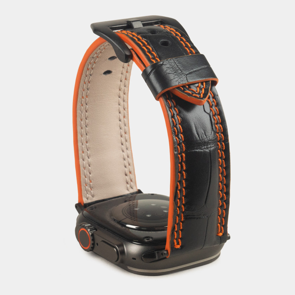 Apple Watch Ultra 49 mm in black alligator leather with orange stitching and edge, with black adapters and buckle | watch case on bottom to see the orange dyed edge