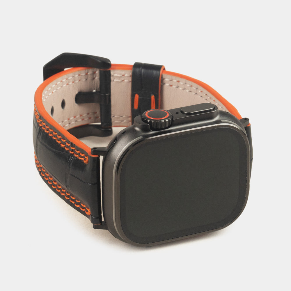 Apple Watch Ultra 49 mm in black alligator leather with orange stitching and edge, with black adapters and buckle | 3/4 front view showing the black watch case and the square scales of the leather
