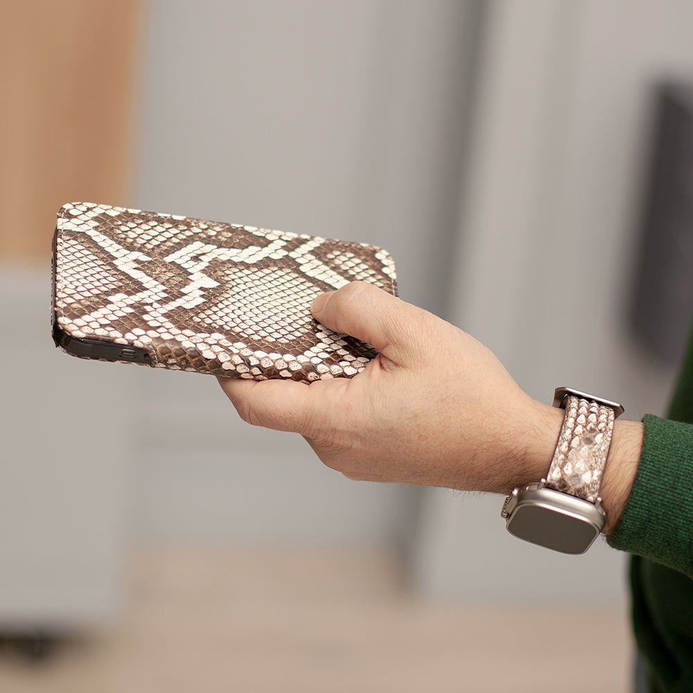 Hand holding iphone in snake skin patterned wallet case with matching strap of apple watch on blurred background